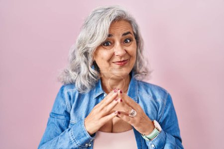 Téléchargez les photos : Middle age woman with grey hair standing over pink background hands together and fingers crossed smiling relaxed and cheerful. success and optimistic - en image libre de droit