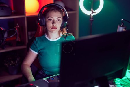 Foto de Redhead woman playing video games with serious expression on face. simple and natural looking at the camera. - Imagen libre de derechos