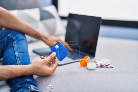 Photo for Young hispanic man using laptop and credit card sitting on sofa at home - Royalty Free Image