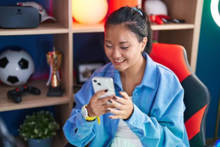 Téléchargez les photos : Jeune femme chinoise streamer souriant confiant en utilisant smartphone à la salle de jeu - en image libre de droit