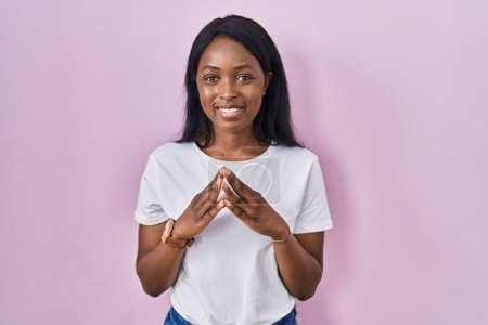 Foto de Mujer joven africana vistiendo casual camiseta blanca manos juntas y los dedos cruzados sonriendo relajado y alegre. éxito y optimismo - Imagen libre de derechos