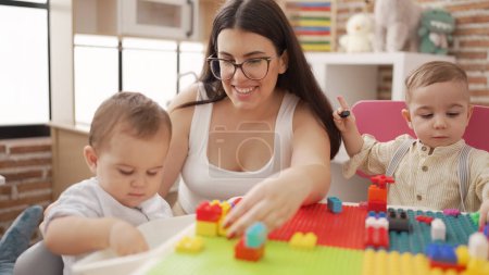 Photo for Teacher and preschool students playing with construction blocks sitting on table at kindergarten - Royalty Free Image