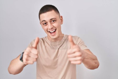 Photo for Young man standing over isolated background approving doing positive gesture with hand, thumbs up smiling and happy for success. winner gesture. - Royalty Free Image
