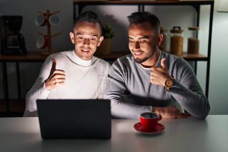 Téléchargez les photos : Homosexual couple using computer laptop doing happy thumbs up gesture with hand. approving expression looking at the camera showing success. - en image libre de droit