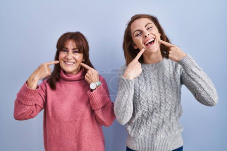 Téléchargez les photos : Mère et fille debout sur fond bleu souriant joyeuse montrant et pointant avec les doigts dents et la bouche. concept de santé dentaire. - en image libre de droit