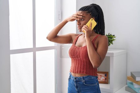Foto de Mujer afroamericana hablando en smartphone con expresión preocupada en casa - Imagen libre de derechos