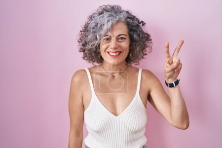 Foto de Mujer de mediana edad con el pelo gris de pie sobre el fondo rosa que muestra y señala hacia arriba con los dedos número dos mientras sonríe confiado y feliz. - Imagen libre de derechos