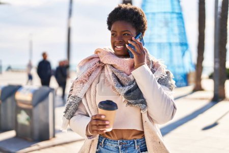 Foto de Mujer afroamericana hablando en el teléfono inteligente tomando café en la calle - Imagen libre de derechos