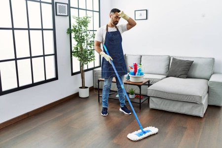 Téléchargez les photos : Young hispanic man tired cleaning floor using mop at home - en image libre de droit