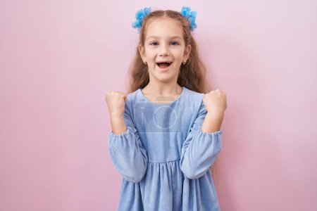 Téléchargez les photos : Young little girl standing over pink background screaming proud, celebrating victory and success very excited with raised arms - en image libre de droit