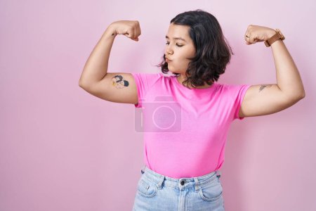 Téléchargez les photos : Jeune femme hispanique debout sur fond rose montrant les muscles des bras souriant fier. concept de fitness. - en image libre de droit