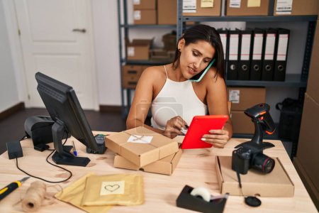 Photo for Young hispanic woman business worker using touchpad and taking on the smartphone at office - Royalty Free Image