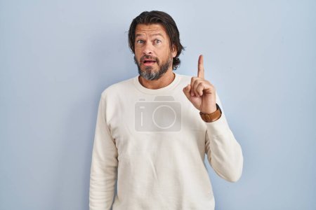 Téléchargez les photos : Handsome middle age man wearing casual sweater over blue background pointing finger up with successful idea. exited and happy. number one. - en image libre de droit