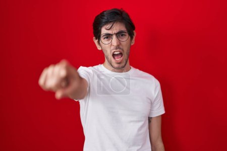 Photo for Young hispanic man standing over red background pointing displeased and frustrated to the camera, angry and furious with you - Royalty Free Image