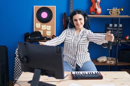 Téléchargez les photos : Young modern girl with blue hair at music studio wearing headphones looking at the camera smiling with open arms for hug. cheerful expression embracing happiness. - en image libre de droit