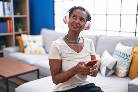 Photo for Middle age african american woman listening to music sitting on sofa at home - Royalty Free Image