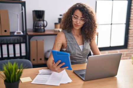 Téléchargez les photos : Jeune belle hispanique femme travailleur d'affaires en utilisant touchpad et ordinateur portable travaillant au bureau - en image libre de droit