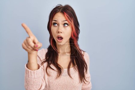 Foto de Young caucasian woman wearing pink sweater over isolated background pointing with finger surprised ahead, open mouth amazed expression, something on the front - Imagen libre de derechos