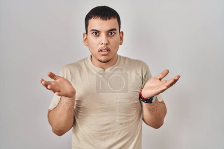 Foto de Hombre árabe joven con camiseta casual despistado y confundido con los brazos abiertos, sin concepto de idea. - Imagen libre de derechos