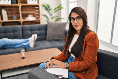 Foto de Young hispanic woman working as psychology counselor relaxed with serious expression on face. simple and natural looking at the camera. - Imagen libre de derechos