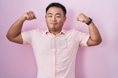 Téléchargez les photos : Chinese young man standing over pink background showing arms muscles smiling proud. fitness concept. - en image libre de droit