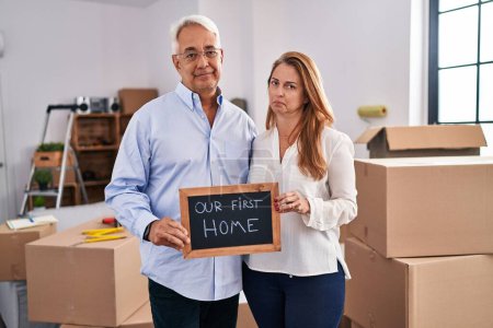 Foto de Middle age hispanic couple moving to a new home holding banner relaxed with serious expression on face. simple and natural looking at the camera. - Imagen libre de derechos