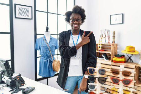 Foto de Mujer joven africana trabajando como gerente en boutique minorista alegre con una sonrisa en la cara señalando con la mano y el dedo hacia el lado con expresión feliz y natural - Imagen libre de derechos