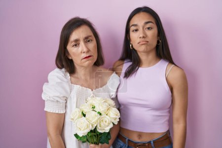 Téléchargez les photos : Hispanic mother and daughter holding bouquet of white flowers looking sleepy and tired, exhausted for fatigue and hangover, lazy eyes in the morning. - en image libre de droit