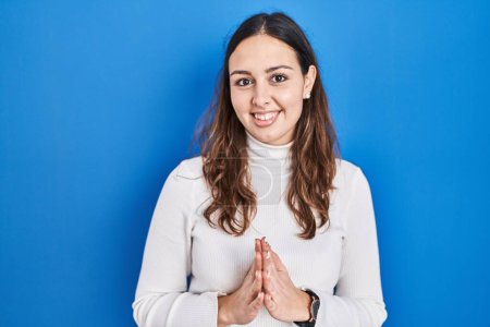 Téléchargez les photos : Jeune femme hispanique debout sur fond bleu mains ensemble et doigts croisés souriant détendu et joyeux. succès et optimisme - en image libre de droit