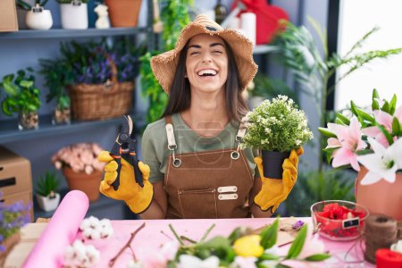 Téléchargez les photos : Young brunette woman working at florist shop smiling and laughing hard out loud because funny crazy joke. - en image libre de droit