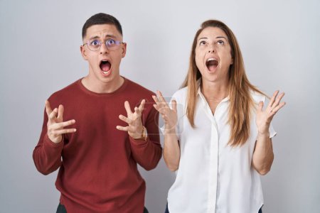 Foto de Mother and son standing together over isolated background crazy and mad shouting and yelling with aggressive expression and arms raised. frustration concept. - Imagen libre de derechos
