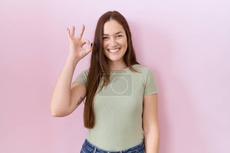 Téléchargez les photos : Belle femme brune debout sur fond rose souriant positif faire ok signe avec la main et les doigts. expression réussie. - en image libre de droit