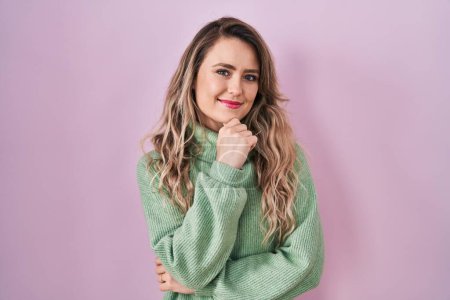 Téléchargez les photos : Young caucasian woman standing over pink background looking confident at the camera smiling with crossed arms and hand raised on chin. thinking positive. - en image libre de droit