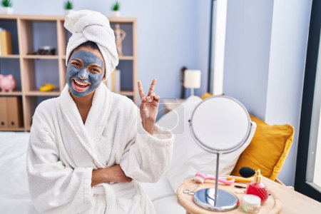 Téléchargez les photos : Hispanic woman with dark hair wearing beauty face mask smiling with happy face winking at the camera doing victory sign. number two. - en image libre de droit