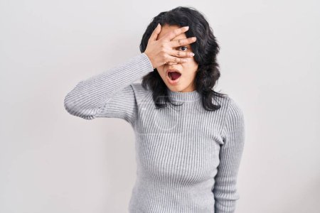 Téléchargez les photos : Hispanic woman with dark hair standing over isolated background peeking in shock covering face and eyes with hand, looking through fingers with embarrassed expression. - en image libre de droit