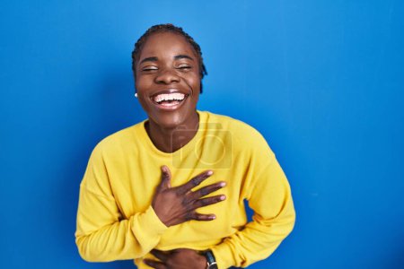 Téléchargez les photos : Beautiful black woman standing over blue background smiling and laughing hard out loud because funny crazy joke with hands on body. - en image libre de droit