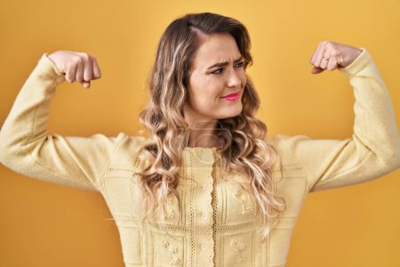 Photo for Young caucasian woman standing over yellow background showing arms muscles smiling proud. fitness concept. - Royalty Free Image
