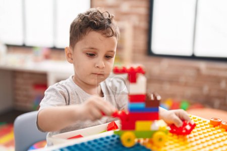 Photo for Adorable hispanic toddler playing with construction blocks sitting on table at kindergarten - Royalty Free Image