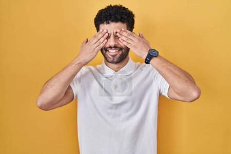 Téléchargez les photos : Arab man standing over yellow background covering eyes with hands smiling cheerful and funny. blind concept. - en image libre de droit