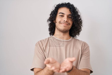 Photo for Hispanic man with curly hair standing over white background smiling with hands palms together receiving or giving gesture. hold and protection - Royalty Free Image