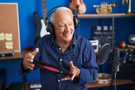 Téléchargez les photos : Senior grey-haired man artist listening to music holding vinyl disc at music studio - en image libre de droit