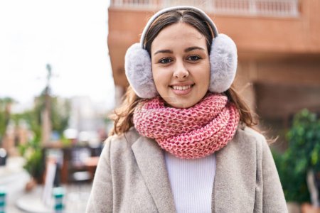 Foto de Young beautiful hispanic woman smiling confident wearing scarf and earmuff at street - Imagen libre de derechos
