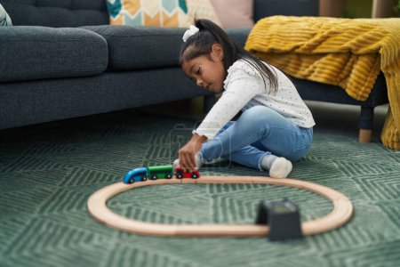 Foto de Adorable chica hispana jugando con el juego del tren sentado en el suelo en casa - Imagen libre de derechos