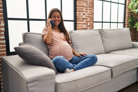 Foto de Young pregnant woman having conversation speaking on the smartphone looking positive and happy standing and smiling with a confident smile showing teeth - Imagen libre de derechos
