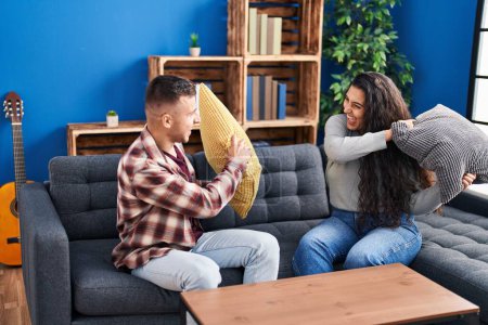 Téléchargez les photos : Man and woman couple fighting with cushion sitting on sofa at home - en image libre de droit