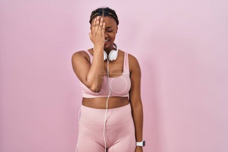 Photo for African american woman with braids wearing sportswear and headphones yawning tired covering half face, eye and mouth with hand. face hurts in pain. - Royalty Free Image