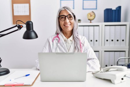 Photo for Middle age grey-haired woman wearing doctor uniform working using computer laptop looking positive and happy standing and smiling with a confident smile showing teeth - Royalty Free Image