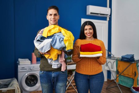 Photo for Young couple holding laundry dirty and clean laundry smiling with a happy and cool smile on face. showing teeth. - Royalty Free Image