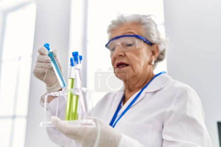 Foto de Mujer mayor de cabello gris con uniforme científico sosteniendo tubos de ensayo en el laboratorio - Imagen libre de derechos