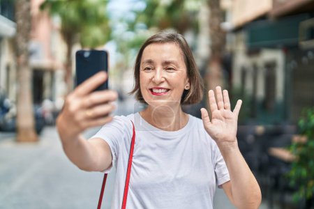 Photo for Middle age hispanic woman doing video call with smartphone looking positive and happy standing and smiling with a confident smile showing teeth - Royalty Free Image